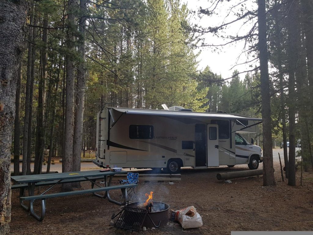 A class c RV parked in front of a campfire at a campground