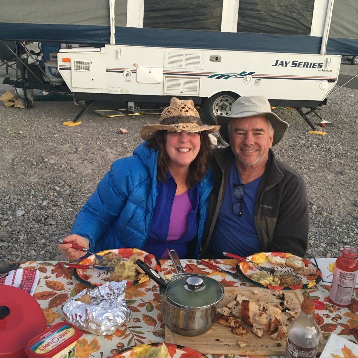 a couple smiles as they eat thanksgiving feast in a campground
