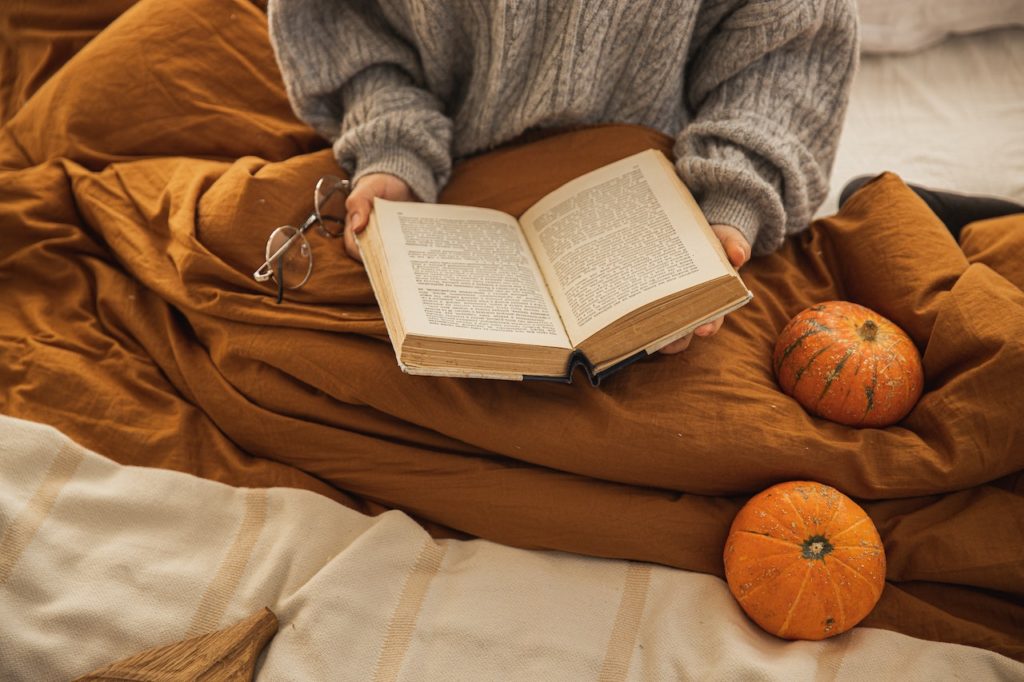 a woman reads a book snuggled up with a blanket in the fall