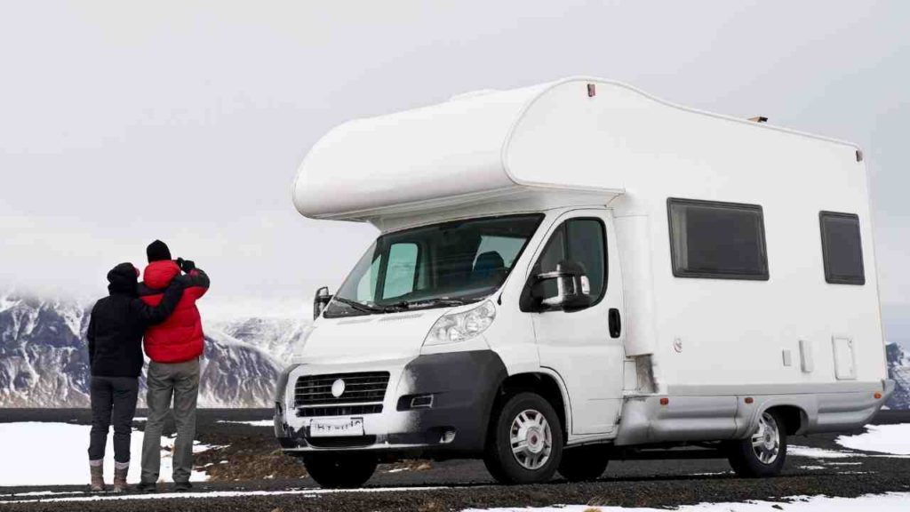 couple taking a photo next to a camper van in the snow.