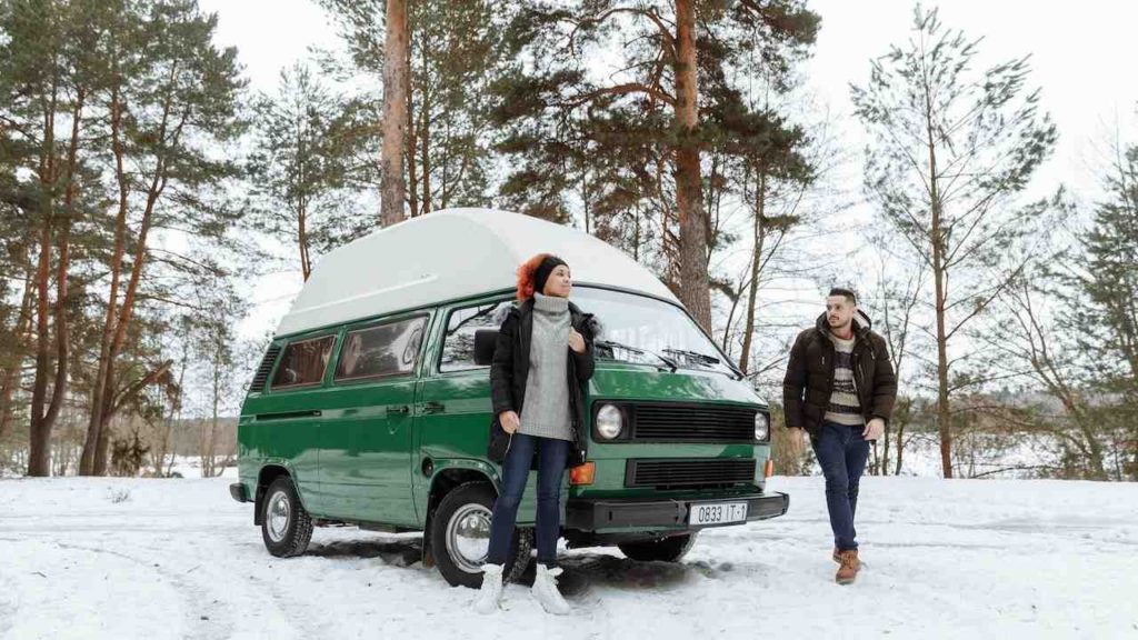 man and woman in front of camper van in the snow.  