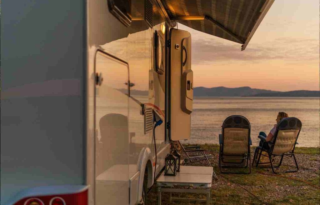 a woman sits next to her RV parked on a lake