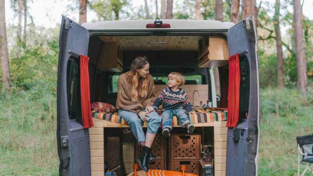 A woman and child sit in the back of a camper van